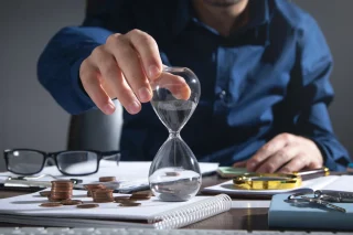 businessman-holding-hourglass-coins-business-objects-desk
